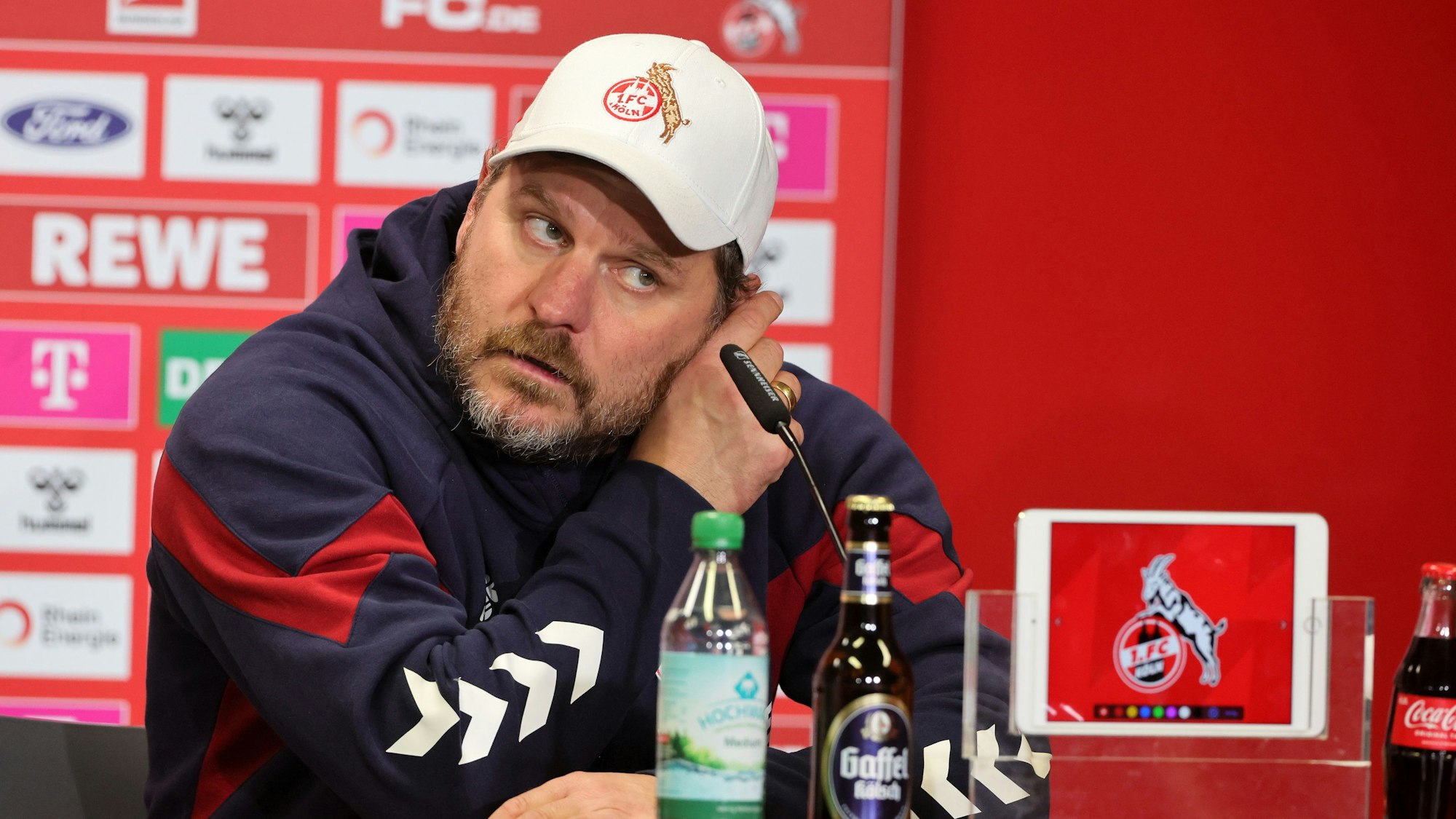 Steffen Baumgart fasst sich bei einer Pressekonferenz des 1. FC Köln ans linke Ohr.