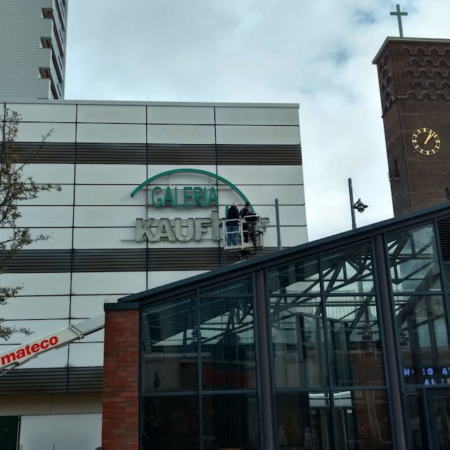 Arbeiter entfernen den Kaufhof-Schriftzug von der Fassade am Wiesdorfer Platz.