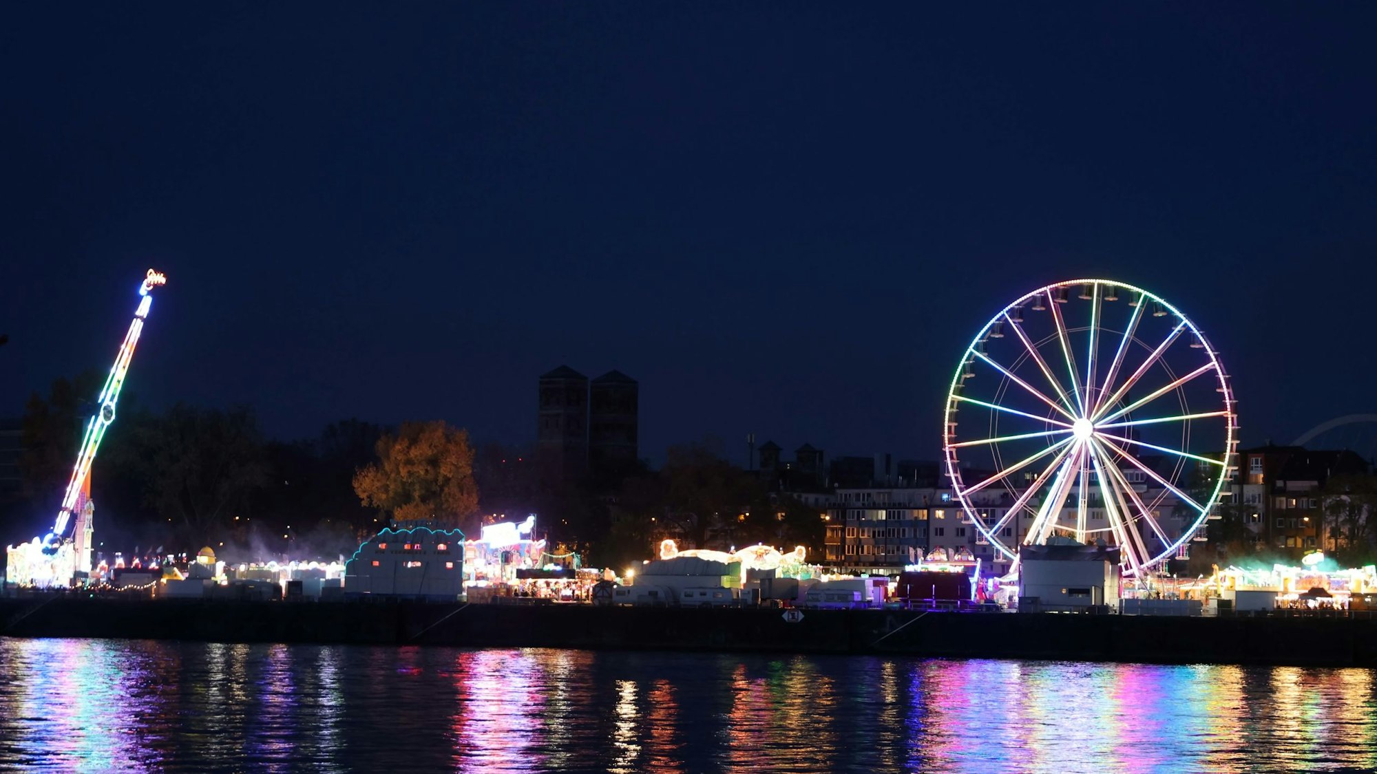 Ein beleuchtetes Riesenrad spiegelt sich im Rhein.