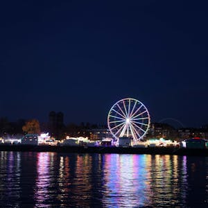 Ein beleuchtetes Riesenrad spiegelt sich im Rhein.