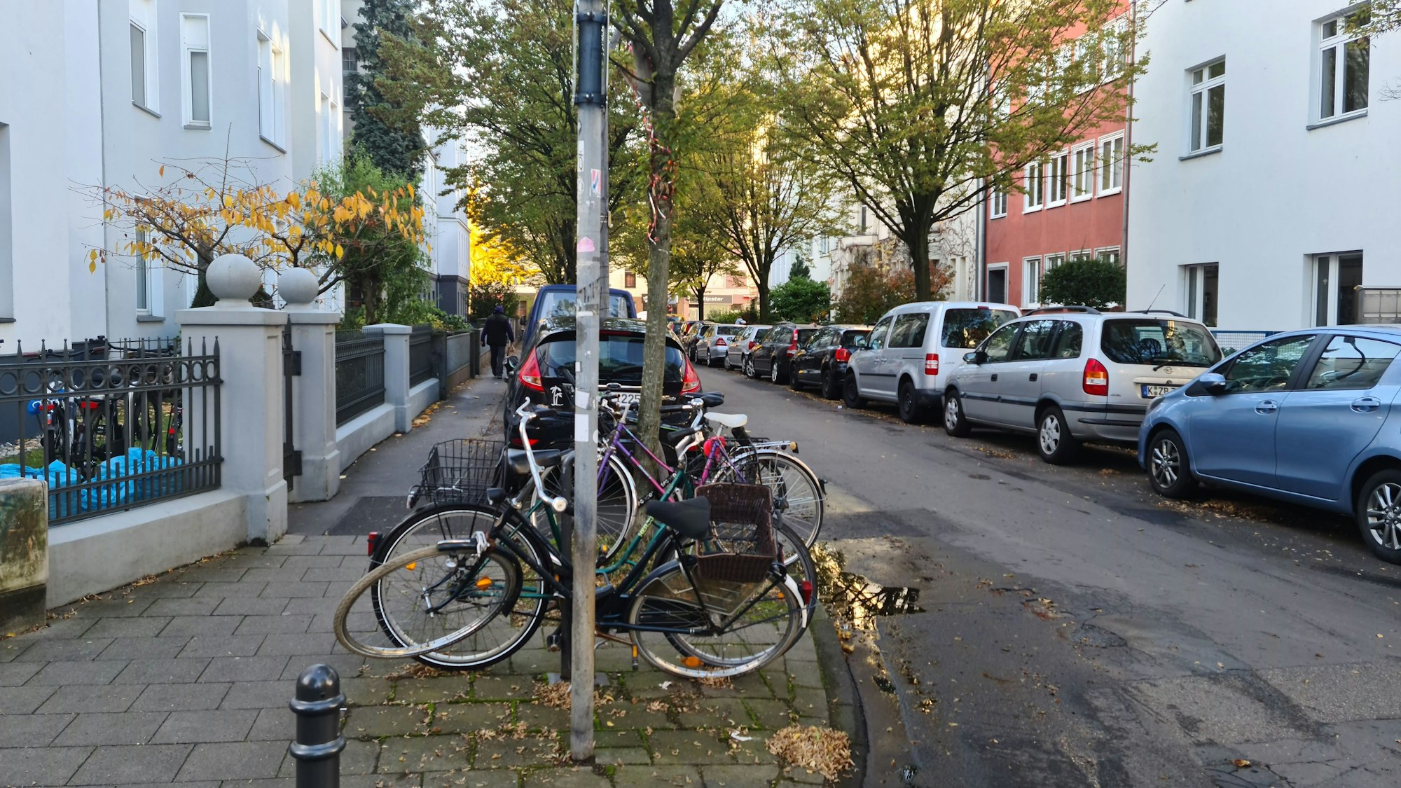 Blick in eine Straße mit parkenden Autos und abgestellten Fahrrädern