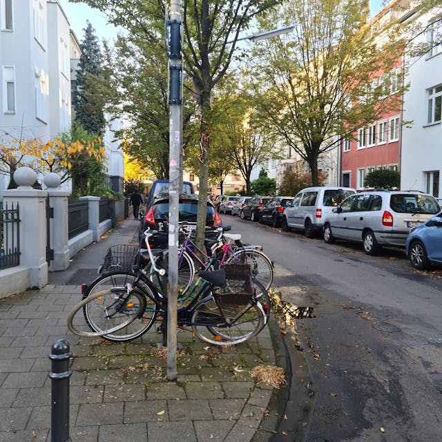 Blick in eine Straße mit parkenden Autos und abgestellten Fahrrädern