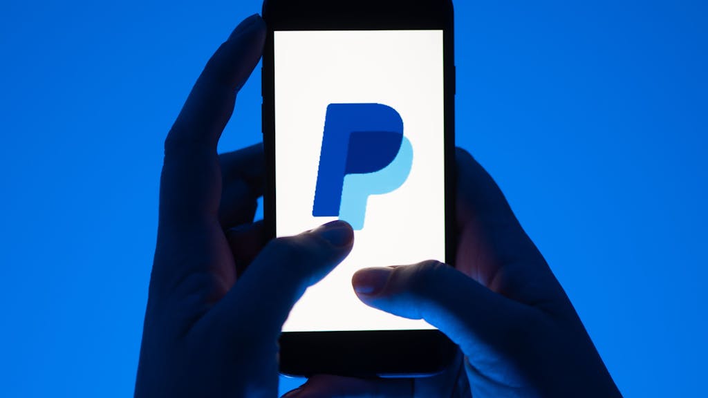 Eine Frau hält ein Smartphone mit dem Logo des Bezahldienstes Paypal.
