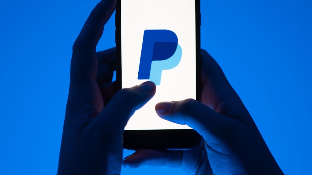 Eine Frau hält ein Smartphone mit dem Logo des Bezahldienstes Paypal.