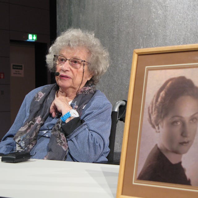 Tamar Dreifuss sitzt an einem Tisch, vorn steht eine gerahmte Fotografie ihrer Mutter.