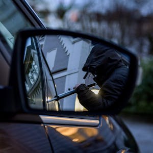 Ein Mann versucht eine Autotür mit einer Metallstange aufzubrechen (gestellte Szene).