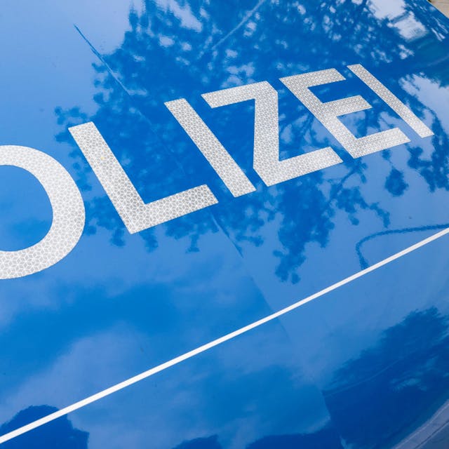 Das Foto zeigt die Motorhaube eines Polizeiwagen, darauf ist in großen weißen Buchstaben auf blauem Grund das Wort „Polizei “zu lesen.