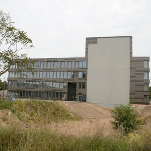 Ein modernes Bürogebäude mit vier Etagen; am Querbau markiert eine graue Fläche den geplanten Hotel-Anbau.