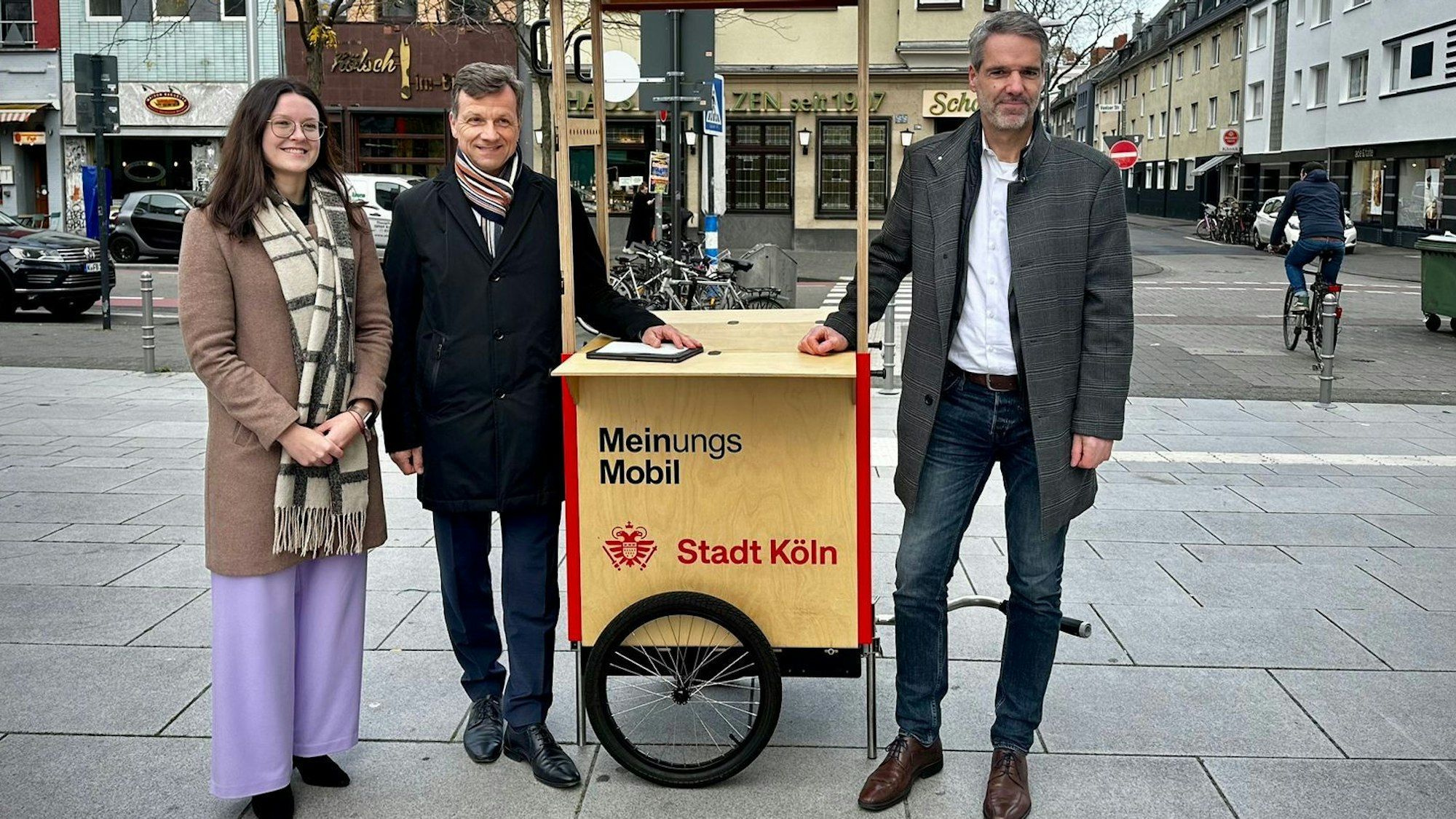 Katharina Pitko, Ascan Egerer und Christian Dörkes stehen mit dem Meinungsmobil der Stadt Köln an der Venloer Straße.