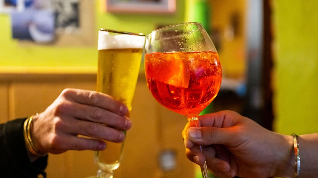In einer Bar stoßen zwei Besucherinnen mit einem Glas alkoholfreiem Bier und einem Glas Aperol Spritz an, hier im Juli 2023 in Berlin.