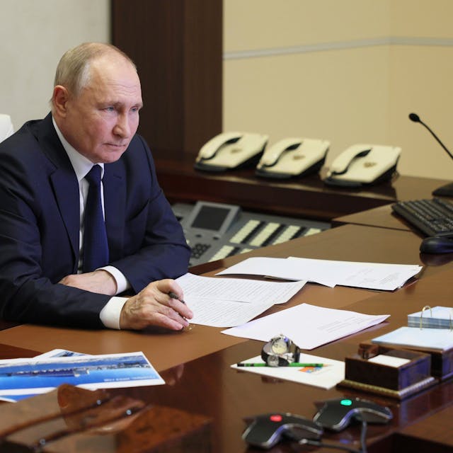 Der russische Präsident Wladimir Putin sitzt einem Schreibtisch, auf dem verschiedene Dokumente liegen und schaut auf einen Computerbildschirm.