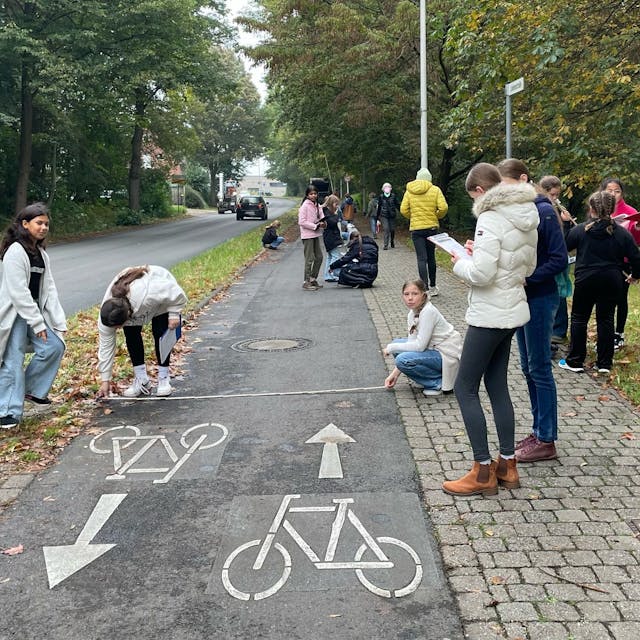 Auf dem Bild sind Schüler zu sehen, die einen Radweg ausmessen.