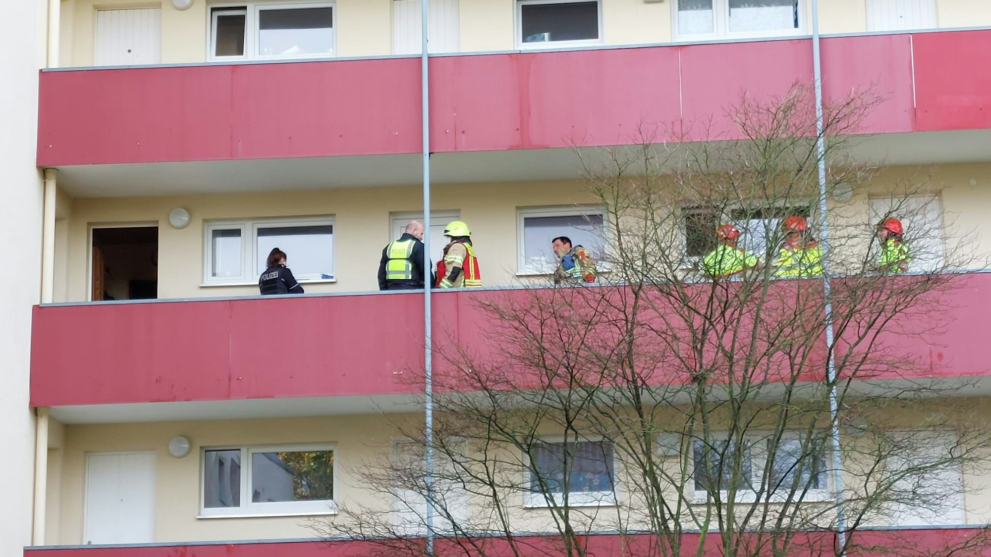 Feuerwehrleute stehen auf dem Gang vor der Wohnung, in der der Brand ausbrach. Es ist ein roter, langer Balkon.