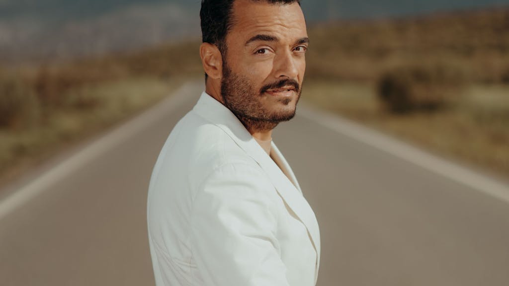 Giovanni Zarrella trägt einen weißen Anzug und blickt auf einer Straße über die Schulter in die Kamera.