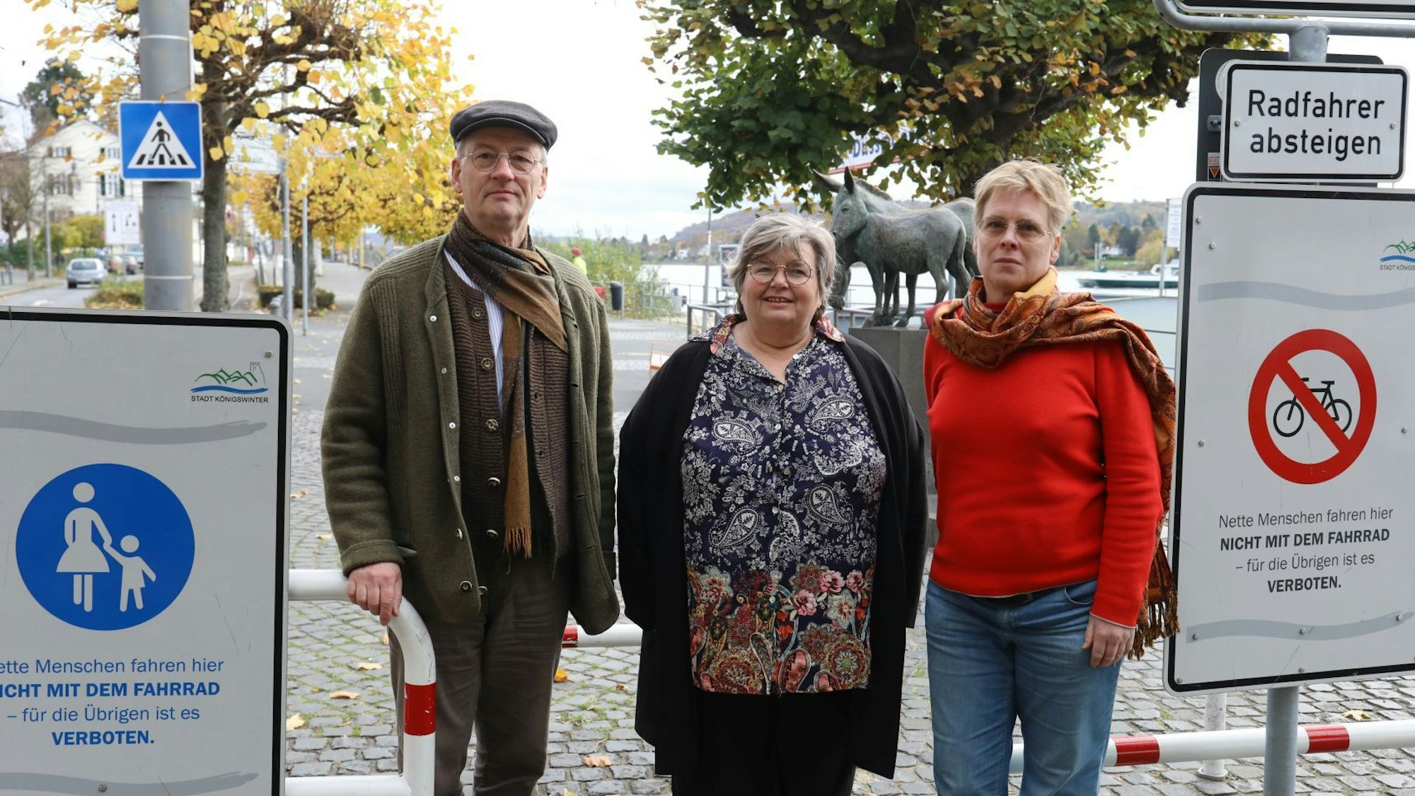 Ein Mann und zwei Frauen stehen auf der Rheinpromenade, auf der in Höhe des Eseldenkmals Schilder das Radfahren untersagen.