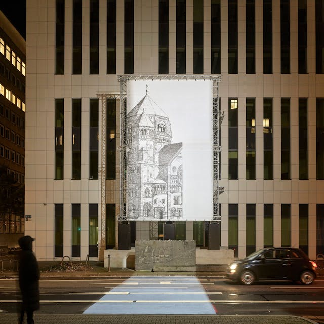 Das Bild zeigt über einem Gedenkstein und vor einem Hochhaus eine Installation. An Gerüsten hängt eine große Lichtinstallation, die den gezeichnet die zerstörte Synagoge in Düsseldorf zeigt.&nbsp;