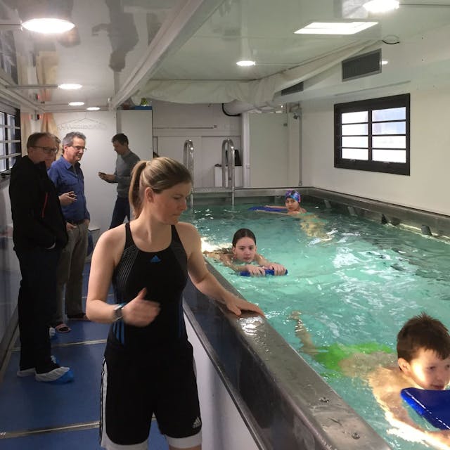 Kinder schwimmen in einem zu einem mobilen Pool umgebauten Container. Eine Lehrerin geht am Beckenrand entlang.