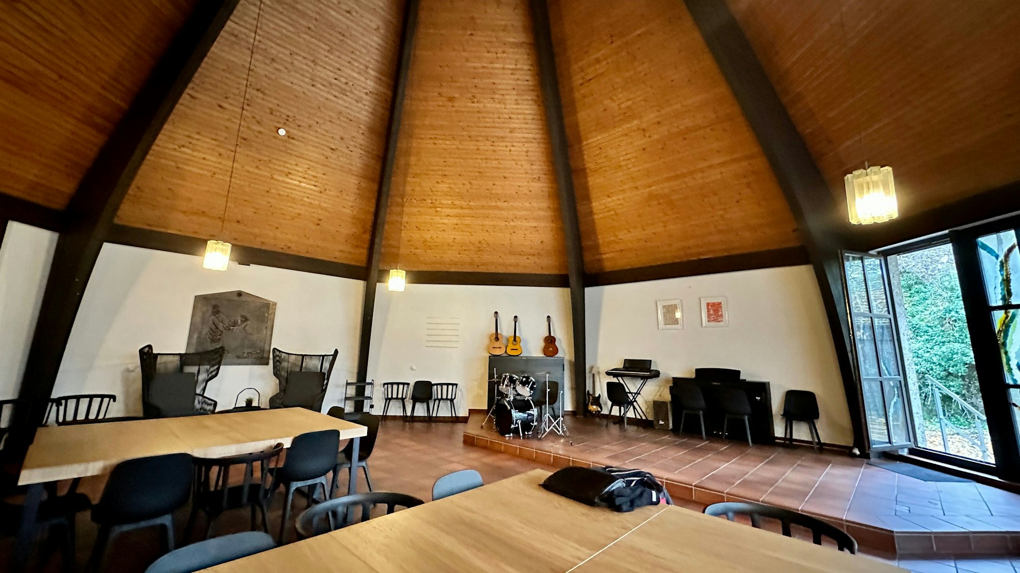 Der luftige Innenraum einer Kirche mit einer hohen holzverkleideten Decke bietet Platz für Tische, Stühle, Gitarren.