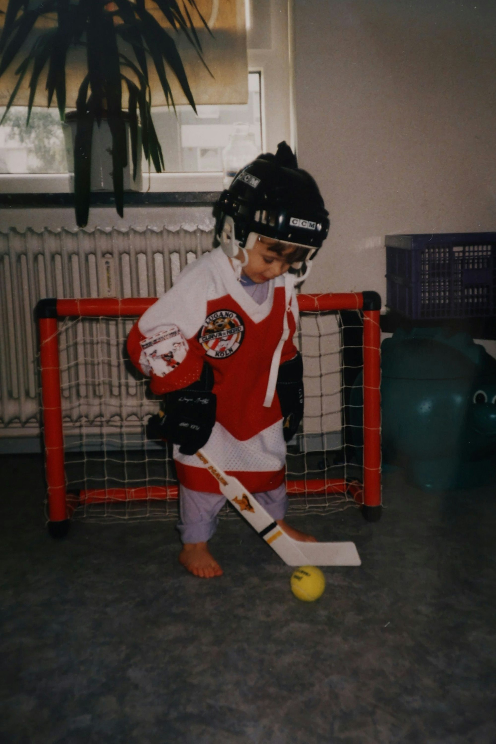 Der kleine Sascha vor einem kleinen Tor, mit Eishockey-Trikot, -Schläger und -Helm.