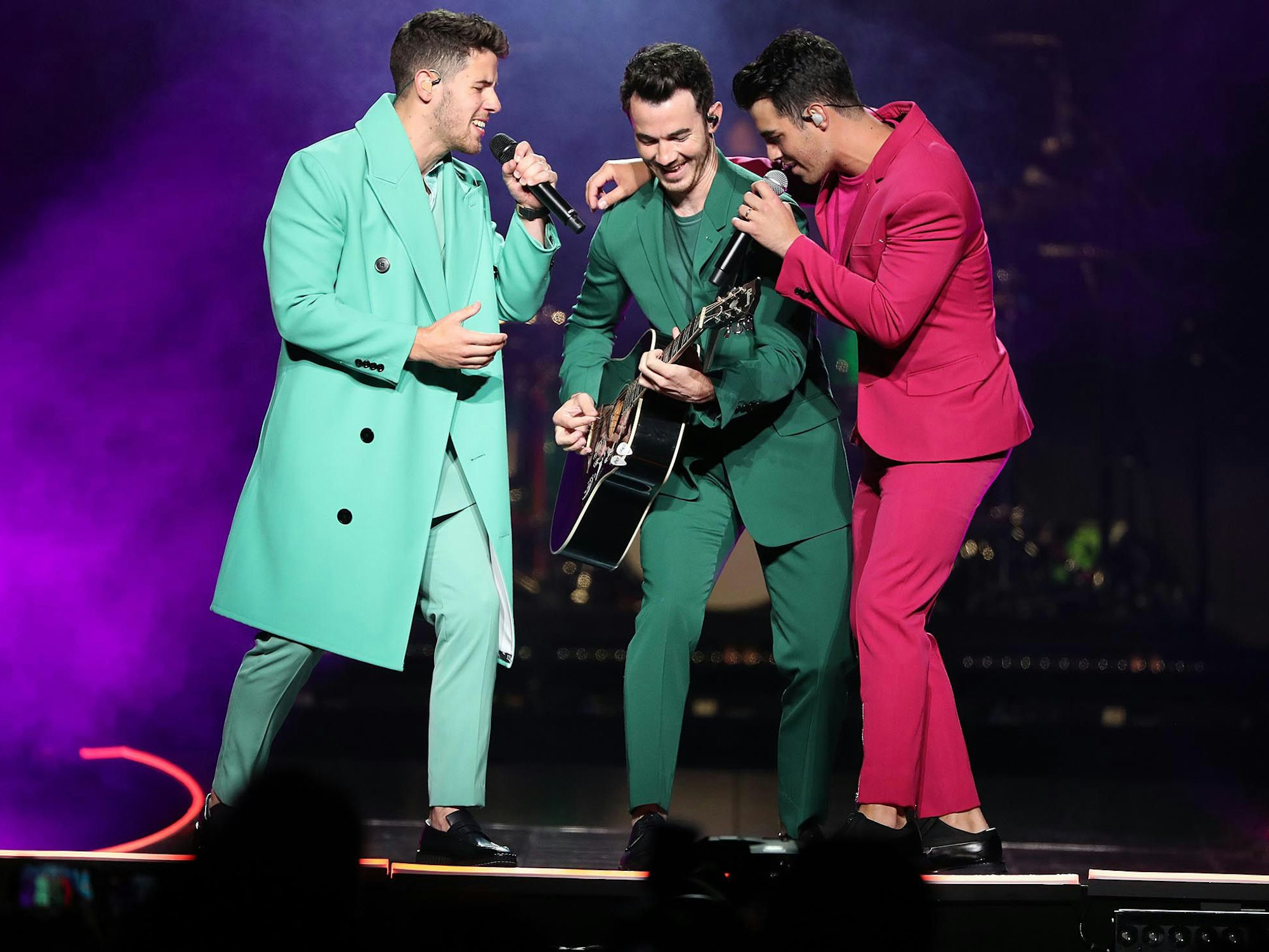 Die Jonas Brothers mit farbigen Anzügen auf der Bühne.