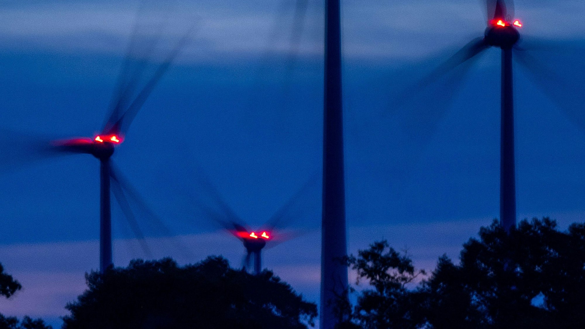 Mit Signallampen beleuchtete Windräder drehen sich nach Sonnenuntergang in einem Windpark.