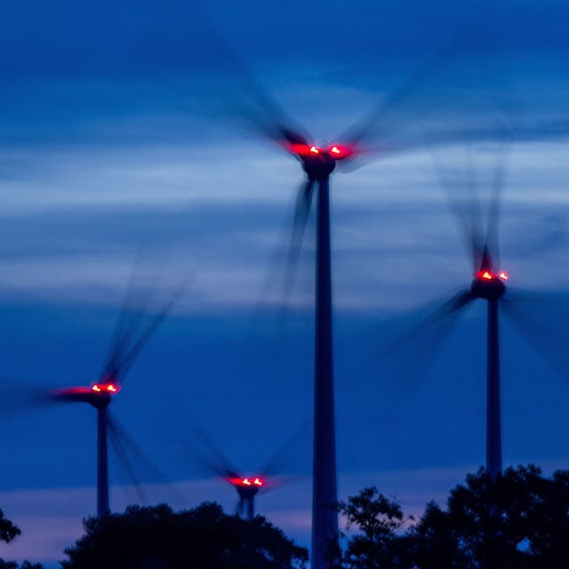 Mit Signallampen beleuchtete Windräder drehen sich nach Sonnenuntergang in einem Windpark.