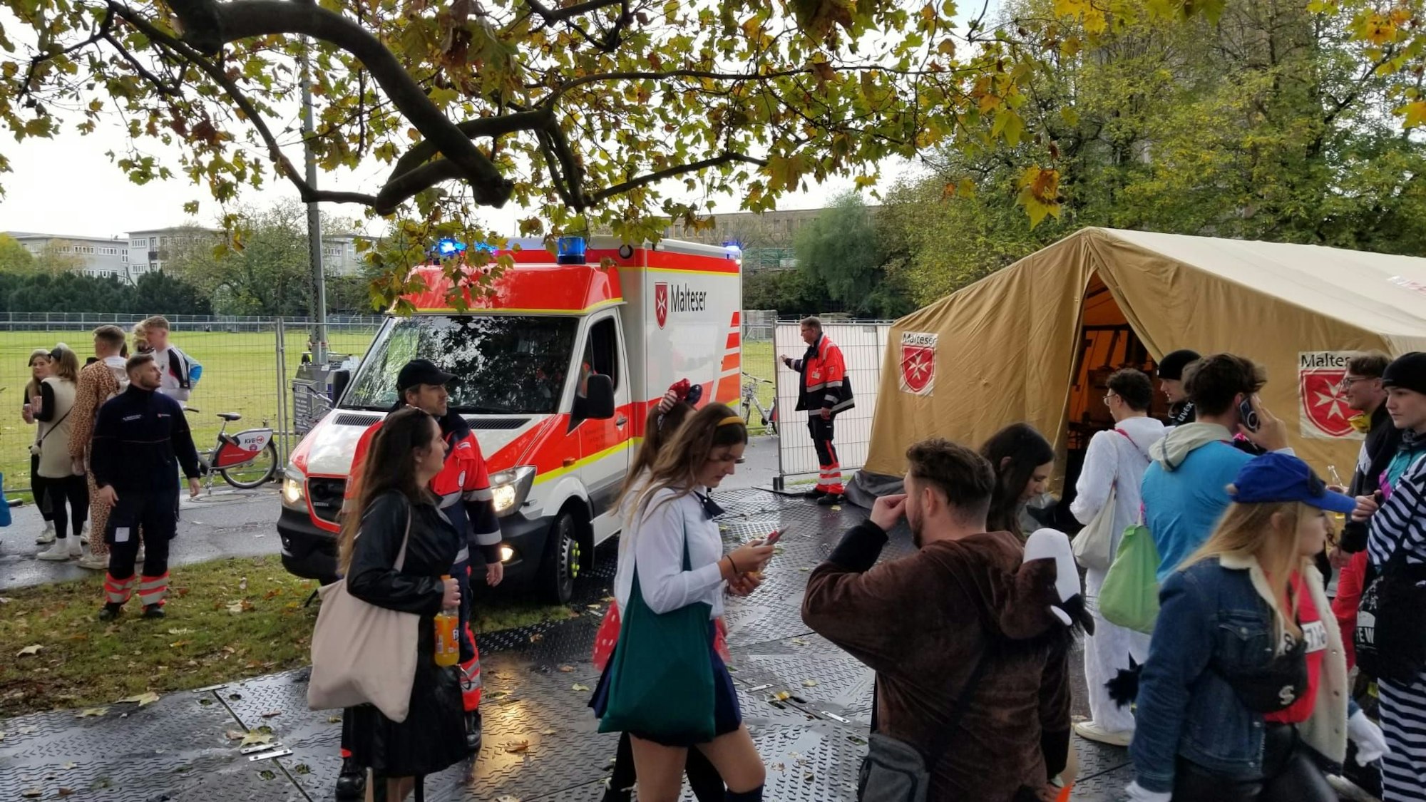 Eine Malteser-Station mit Krankenwagen, davor sind zahlreiche Kostümierte zu sehen.