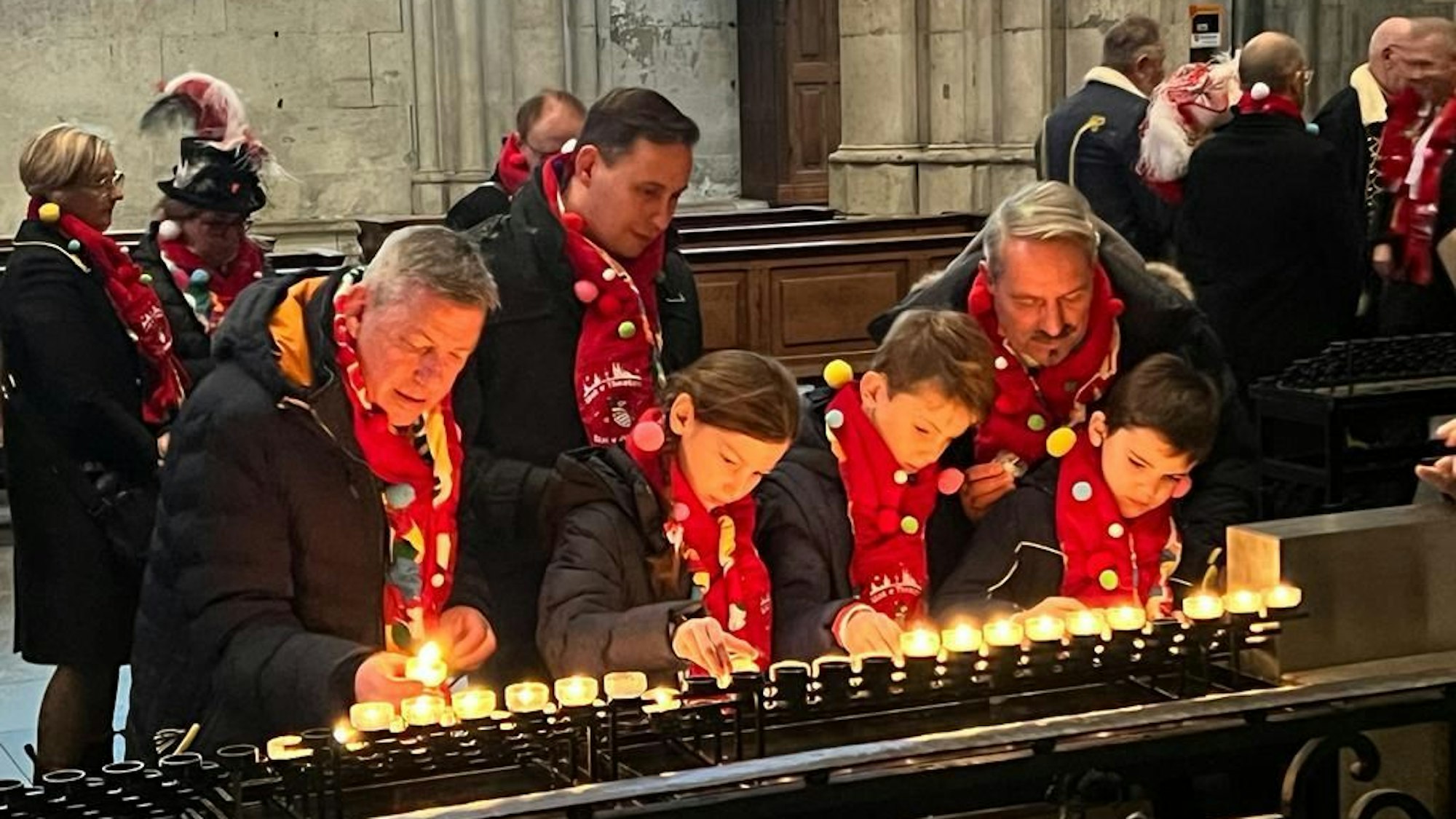 Drei Erwachsene und drei Kinder zünden im Kölner Dom Kerzen an.