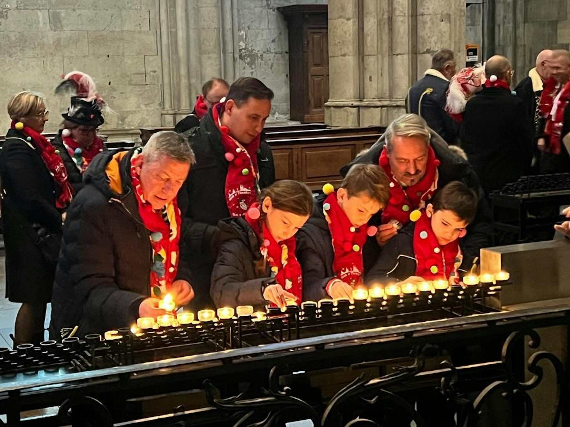 Drei Erwachsene und drei Kinder zünden im Kölner Dom Kerzen an.