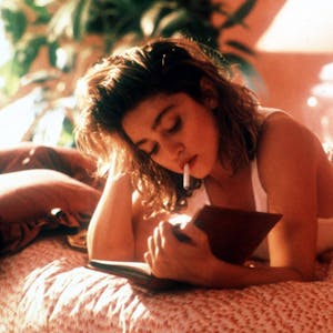 Madonna als Susan, rauchend im Bett, während sie ein Buch liest.