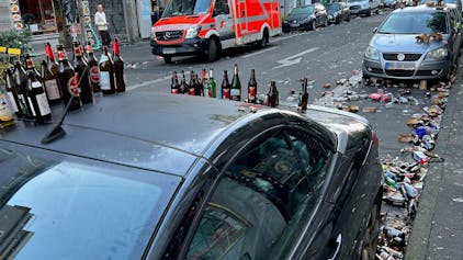 Bierflaschen stehen auf dem Dach eines geparkten Autos, auch auf der Straße liegen Berge von Glasflaschen.