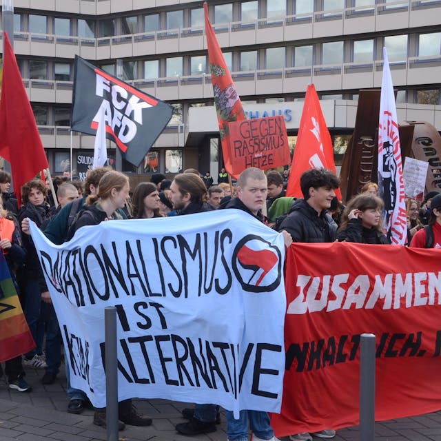 Menschen mit Spruchbändern und Fahnen auf der Straße vor dem Troisdorfer Rathaus.