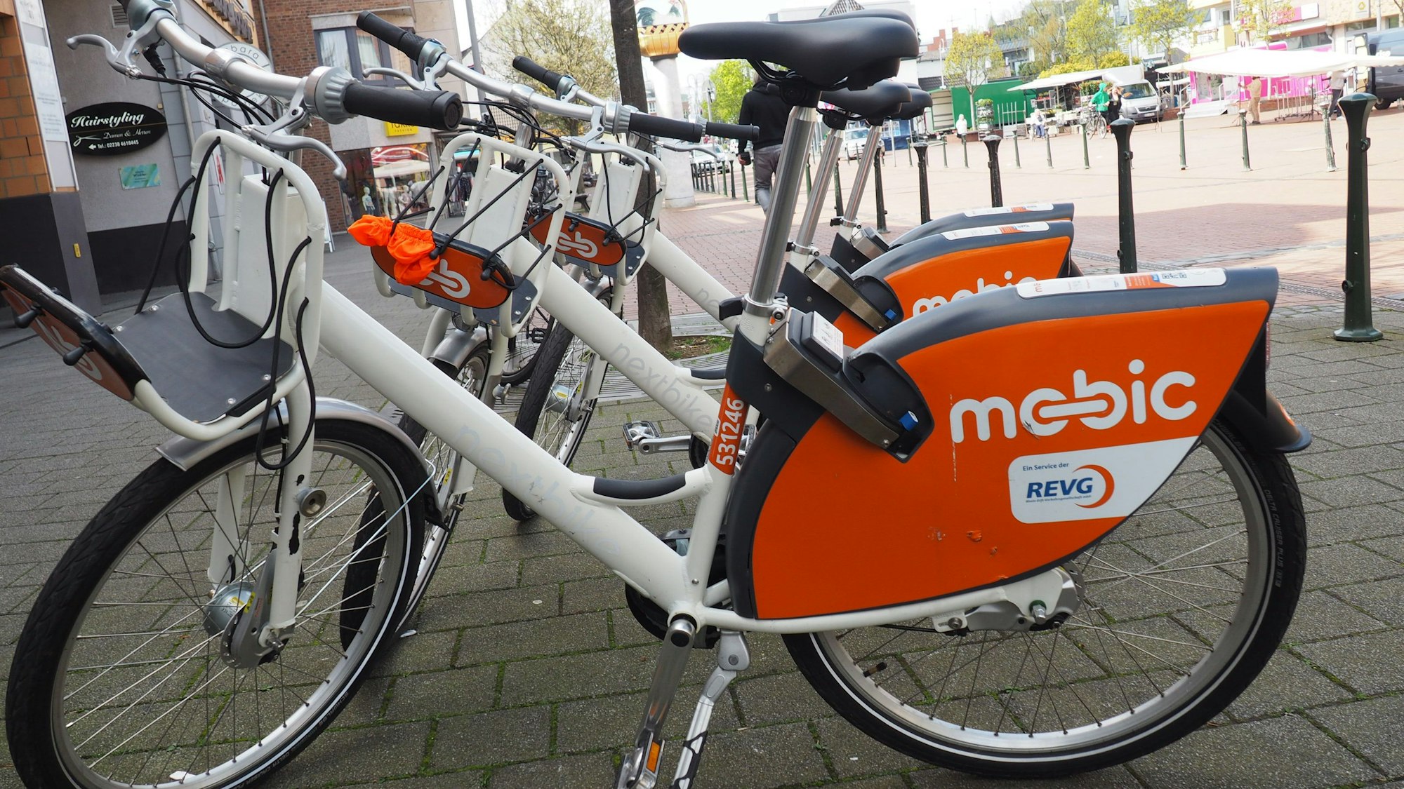 Zu sehen sind weiße Mietfahrräder mit dem orangefarbenen Schriftzug Mobic.