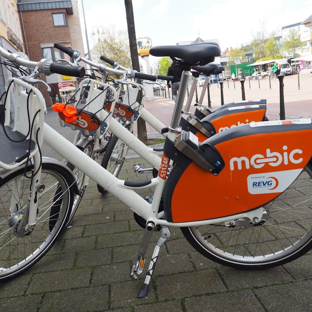 Zu sehen sind weiße Mietfahrräder mit dem orangefarbenen Schriftzug Mobic.
