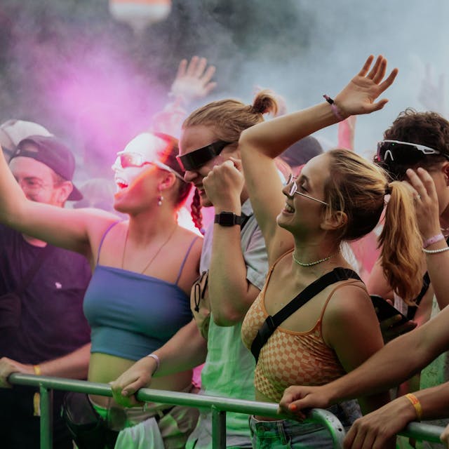 Menschen stehen an einer Absperrung vor einer Bühne, werfen die Hände in die Luft und feiern zur Musik vom Open-Air-Festival.