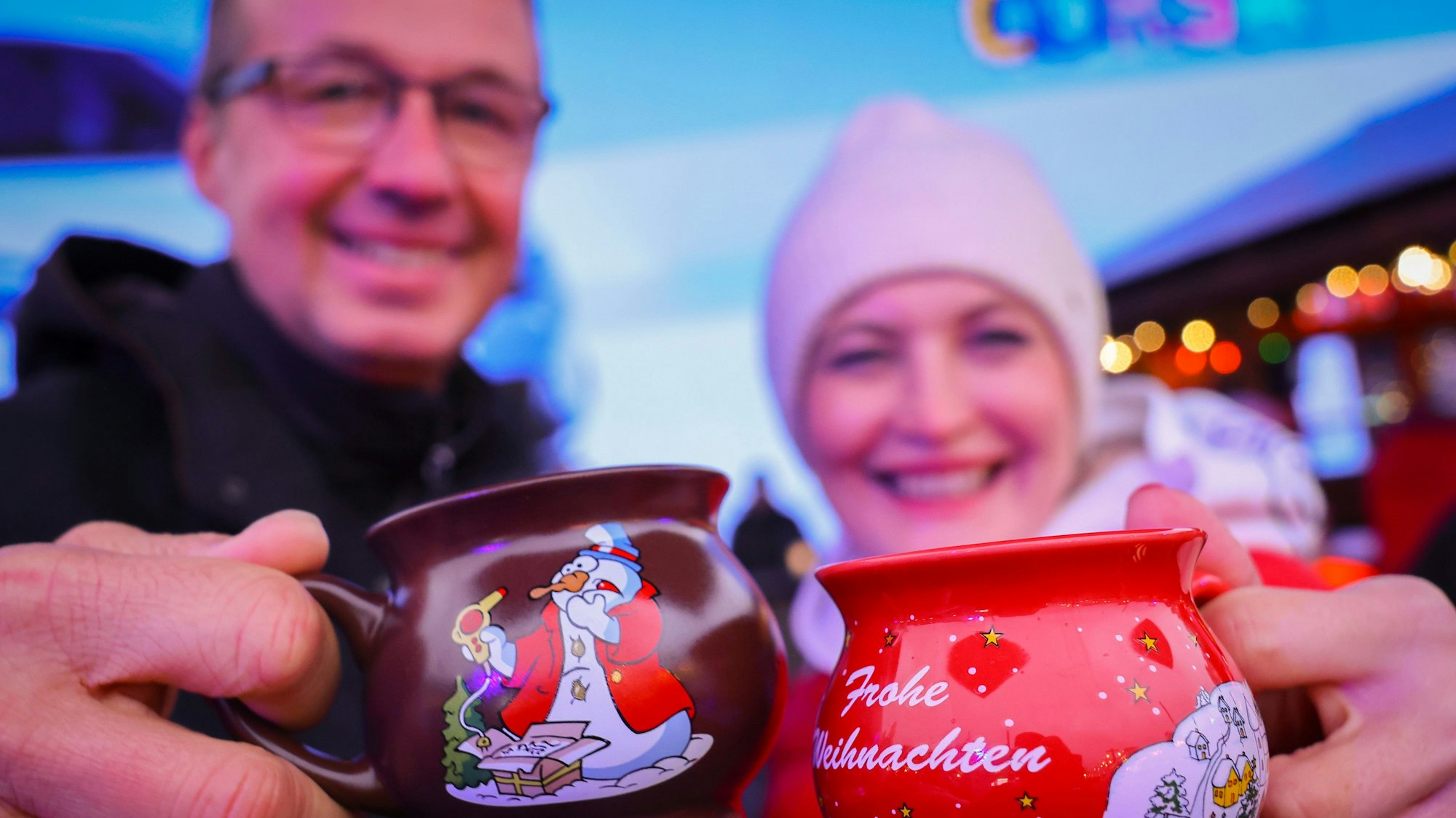 Ein Paar hält zwei Tassen mit heißem Glühwein kurz nach der Eröffnung eines Weihnachtsmarktes in den Händen und stößt an.