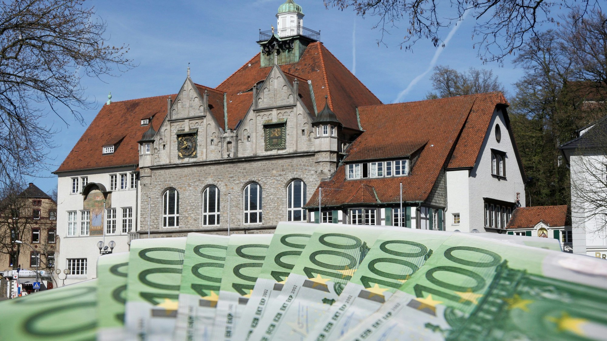 Das Foto zeigt das Historische Rathaus Gladbach und ein Bündel 100-Euro-Scheine.