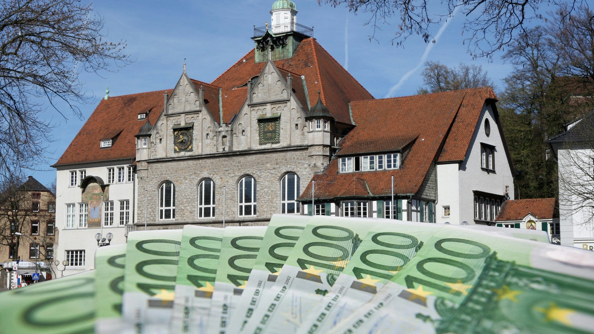 Vor dem Bergisch Gladbacher Rathaus sind aufgefächerte Geldscheine zu sehen.