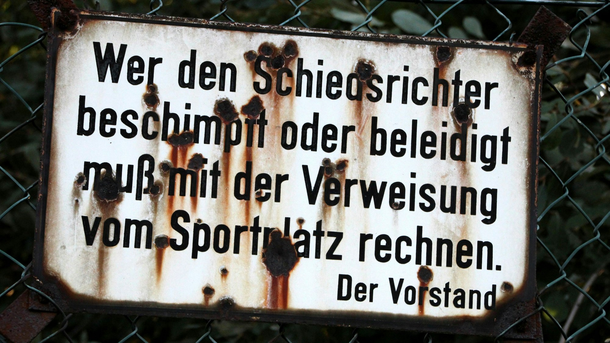 Ein verwittertes Schild, auf dem steht: „Wer den Schiedsrichter beschimpft oder beleidigt muß mit der Verweisung vom Sportplatz rechnen.“