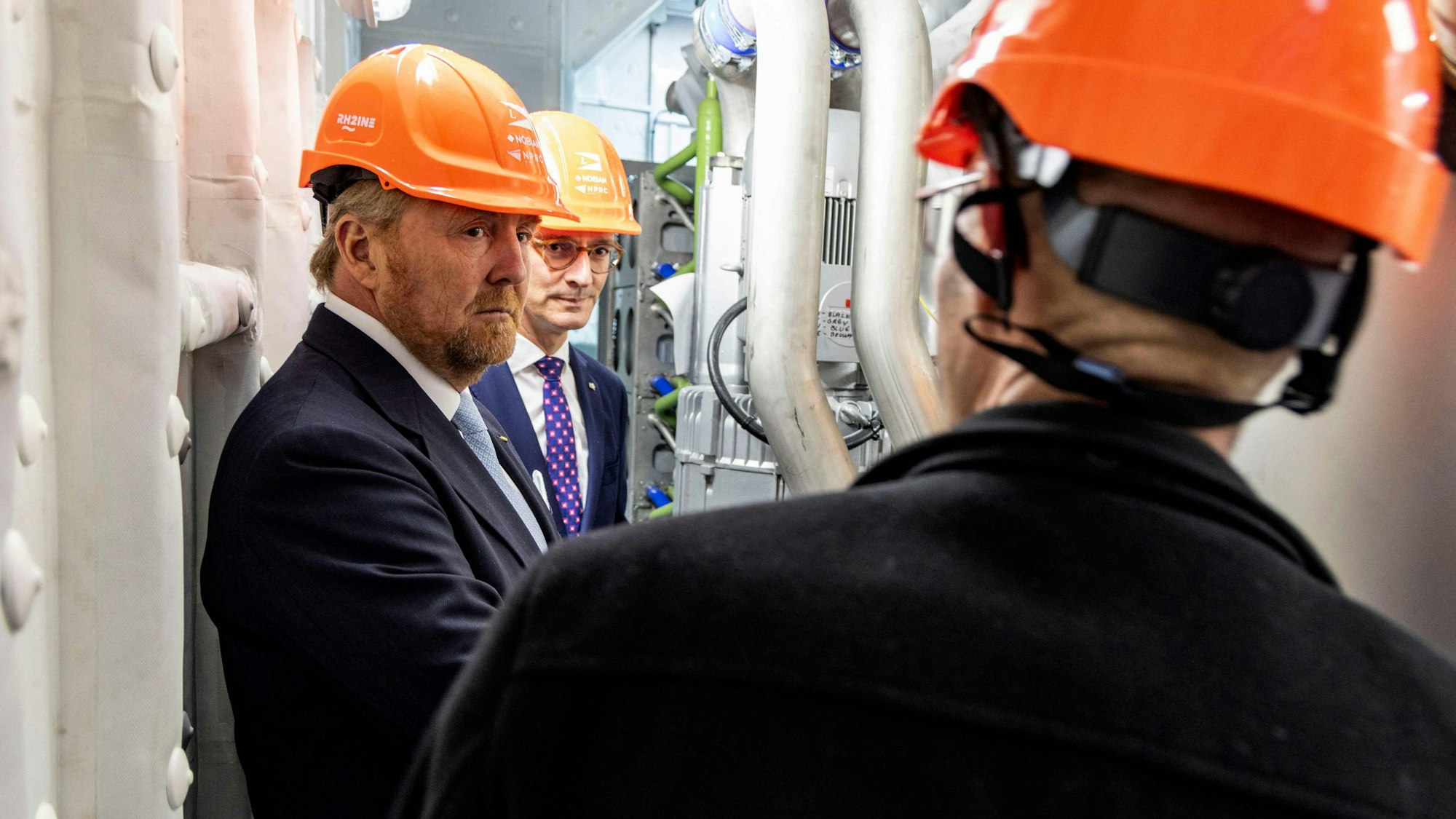 King Willem-Alexander of the Netherlands (L) and North Rhine-Westphalia's State Premier Hendrik Wuest (C) stand in the engine room of a hydrogen ship in the port of Duisburg, western Germany on November 14, 2023. The Dutch King and North Rhine-Westphalia's Prime Minister visit various companies and institutions. (Photo by Christoph Reichwein / POOL / AFP)