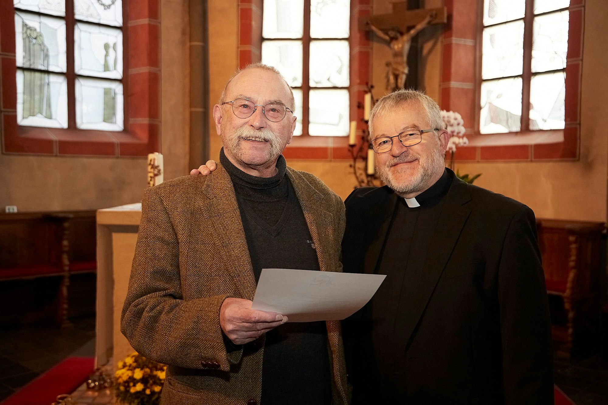 Die Entpflichtungsurkunde hält Pfarrer Philipp Cuck in der Hand. Regionaldekan Pater Wieslaw Kaczor steht neben ihm.