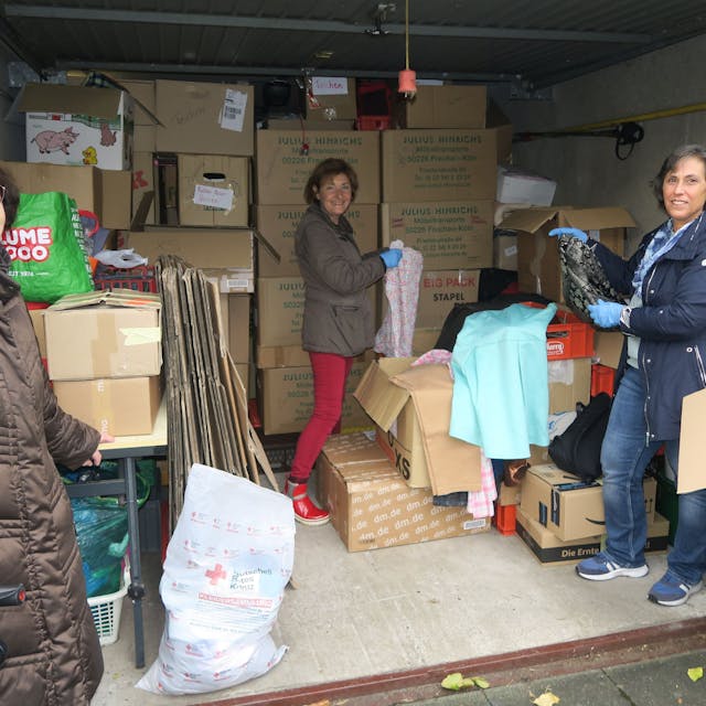 Drei Frauen stehen in einer Garage, die voll ist mit Kartons.