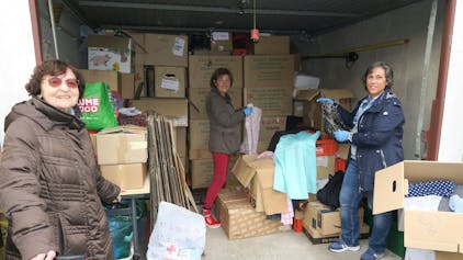Drei Frauen stehen in einer Garage, die voll ist mit Kartons.
