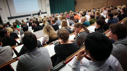 Studierende sitzen in einem Hörsaal der Universität und verfolgen eine Vorlesung.&nbsp;