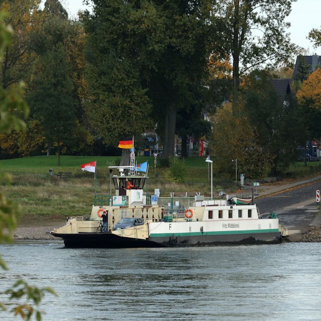 Die Rheinfähre „Fritz Middelanis“ liegt am Anlieger in Leverkusen-Hitdorf. Drumherum sind herbstlich gefärbte Bäume zu sehen.