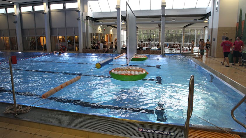 Das Aquarena-Hallenbad in Neunkirchen: Wasser glitzert im Becken, Menschen stehen am Beckenrand.
