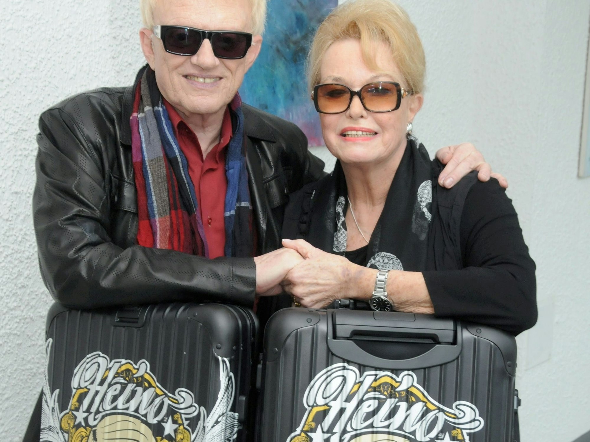 Das Bild zeigt Heino und Hannelore, wie sie auf zwei Koffern Händchen halten.