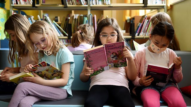 Mädchen sitzen auf einem bunten Podest und lesen in Büchern.