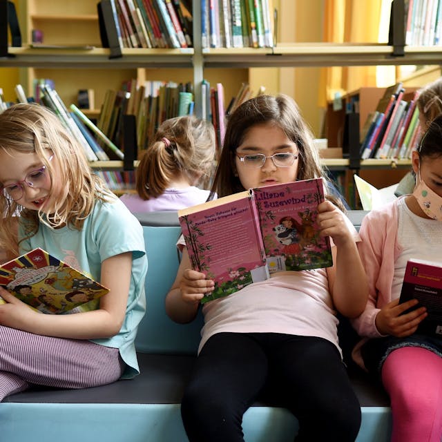 Mädchen sitzen auf einem bunten Podest und lesen in Büchern.