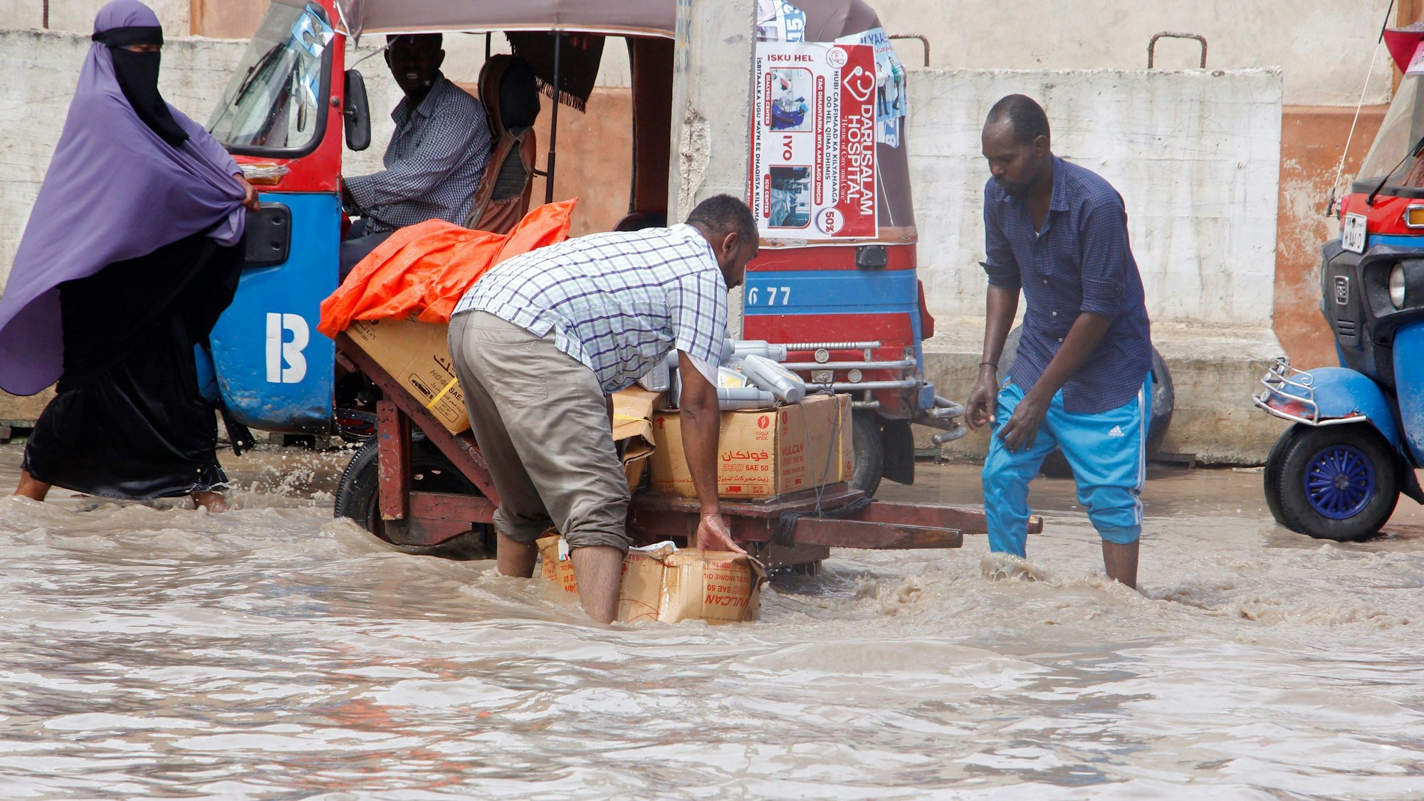 Somalier überqueren eine überflutete Straße. Das Wasser steht ihnen bis zu den Knien.